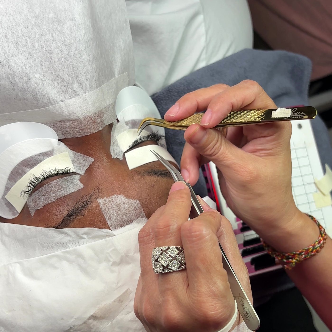 Close-up of a volume lash fan being placed with gold tweezers